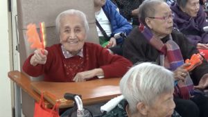 While the volunteers are giving impromptu performances to the elderly, such as playing Chinese music and singing, the elderly are getting a big laugh. The atmosphere is filled with warmth and excitement.
