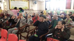 The volunteers are leading the elderly to do fitness exercise. 