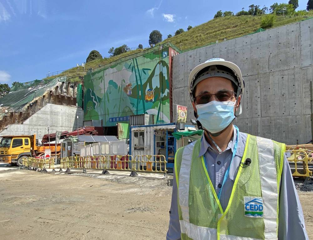 Senior Explosives Officer of the GEO, Mr NG Siu-ming, says that blasting is necessary for many works projects in Hong Kong. An example is the relocation of Sha Tin Sewage Treatment Works to caverns in Nui Po Shan of A Kung Kok behind him.