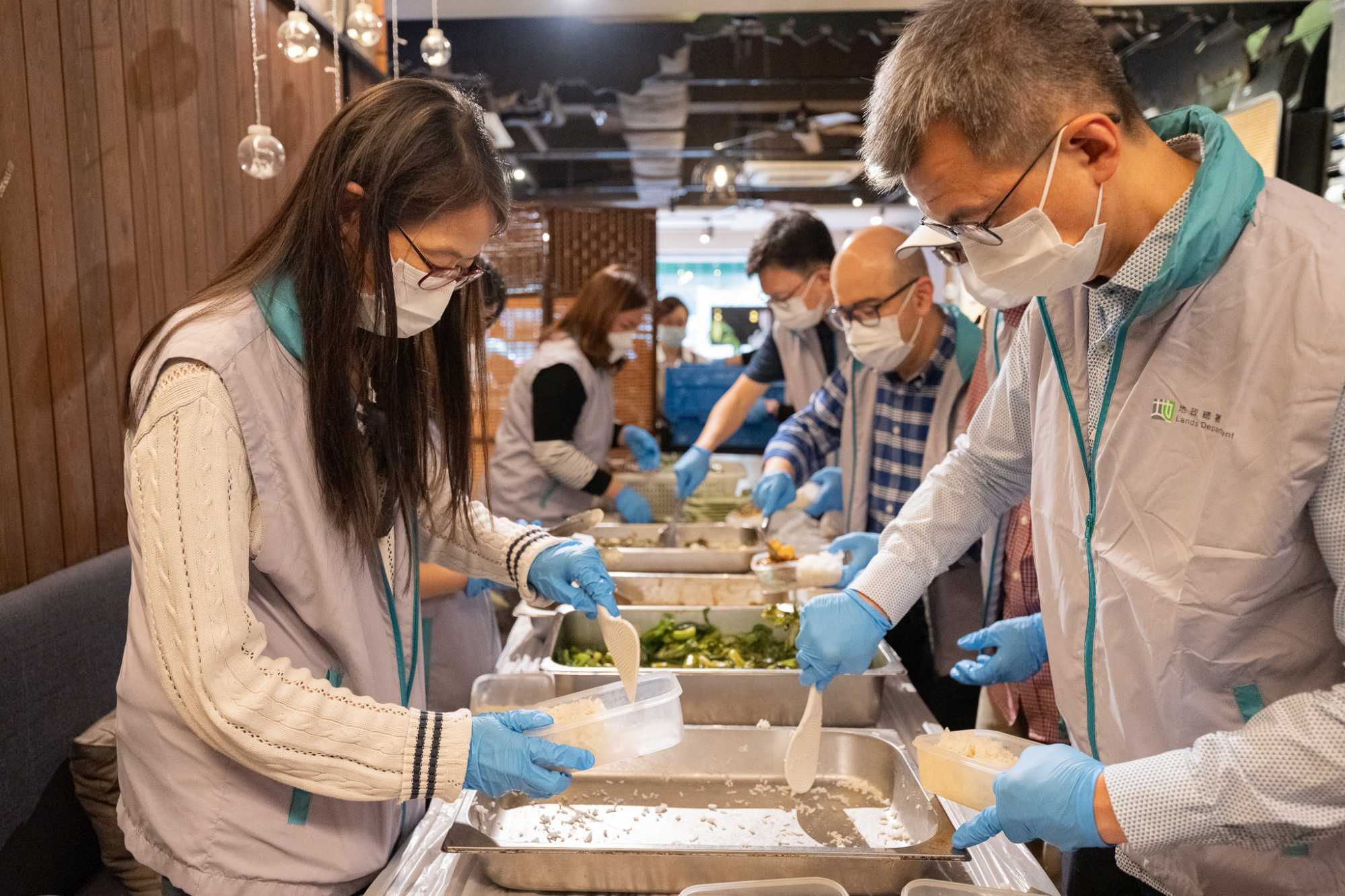 地政總署署長黎志華（右一）和發展局副秘書長（規劃及地政）潘偉榮（右二）與地政總署同事參與派福飯義工服務，為有需要長者準備餐膳。