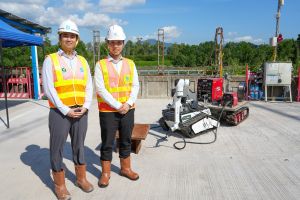 發展局助理秘書長（計劃管理）羅梓馨（右）和渠務署工程師李澤祖（左）介紹「元朗防洪壩及明渠改善計劃」工程中應用的燒焊機械人及遙控天秤系統。