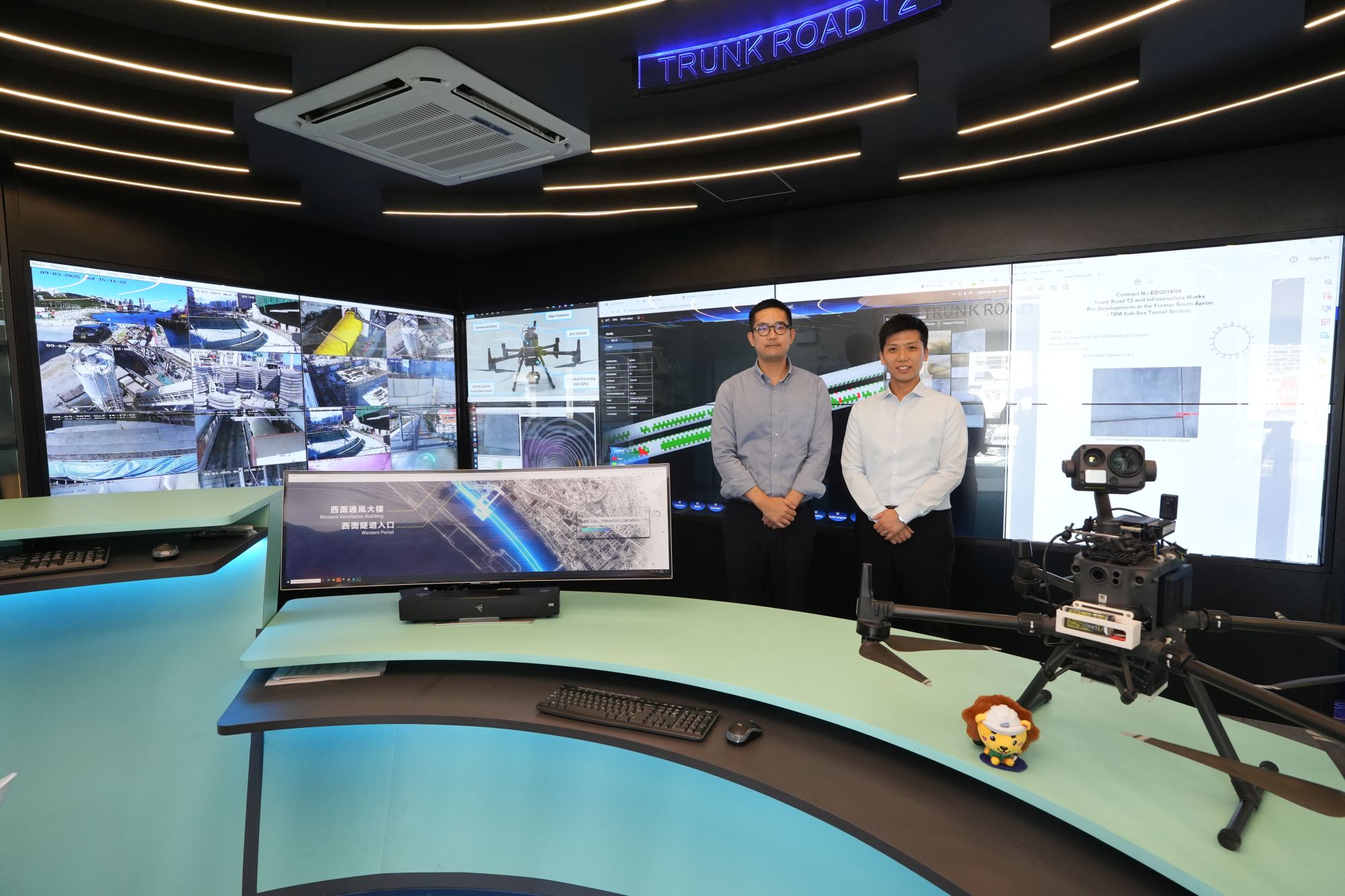 發展局助理秘書長（計劃管理）羅梓馨（右）和土木工程拓展署工程師馬浩斌（左）介紹土木工程拓展署在「T2主幹路及茶果嶺隧道」工程中應用的鑽孔機械人和「智能隧道質量檢測系統」。