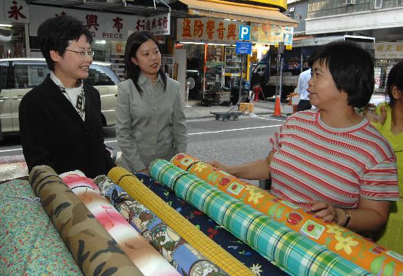 Accompanied by the Sham Shui Po District Officer, Miss May Chan (centre), the Secretary for Development, Mrs Carrie Lam, chats with a cloth stall operator at Ki Lung Street.