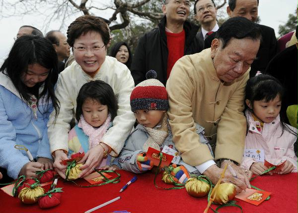 The Secretary for Development, Mrs Carrie Lam, joins Chairman of Heung Yee Kuk, Mr Lau Wong-fat, and children in writing new year wishes on paper cards before throwing them onto the new model wishing tree in Lam Tsuen, Tai Po.