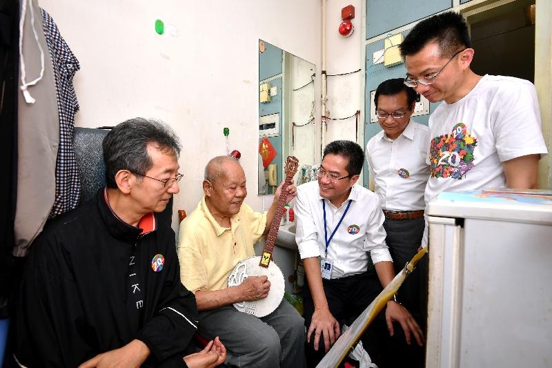 Accompanied by the Chairman of the Sham Shui Po District Council, Mr Ambrose Cheung (first left), the Secretary for Development, Mr Michael Wong (centre); the Director of Buildings, Mr Cheung Tin-cheung (first right); and the Managing Director of the Urban Renewal Authority, Mr Wai Chi-sing (second right), today (July 28) visited a singleton elderly resident living in Un Chau Estate to learn more about his living conditions and needs. Photo shows them listening to the elderly resident play a musical instrument during the visit.