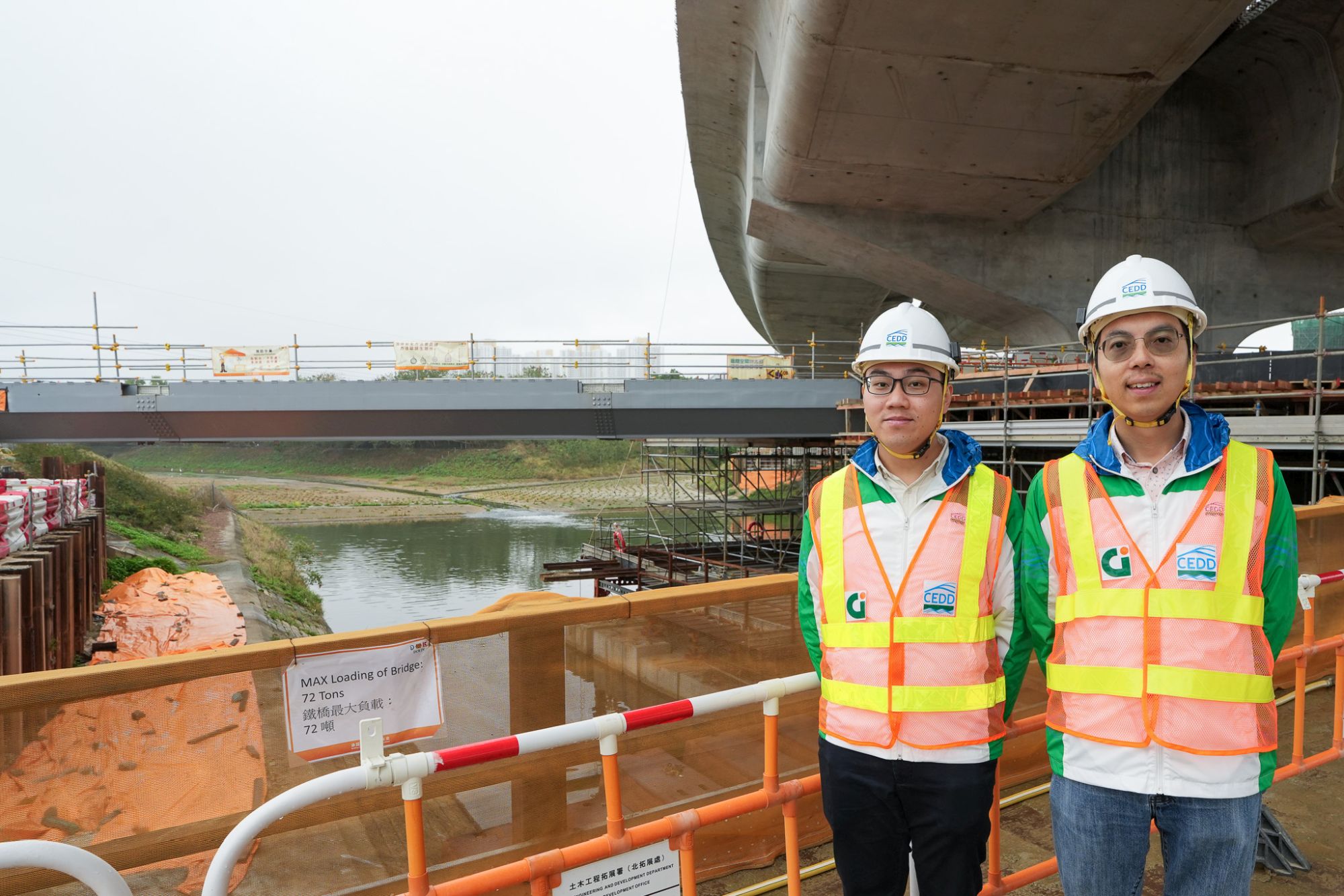 土木工程拓展署高级工程师梁伟乐（右）和土木工程拓展署工程师郑允健（左）于其中一条位于粉岭梧桐河，以S960超高强钢建造的行人天桥附近介绍有关项目。