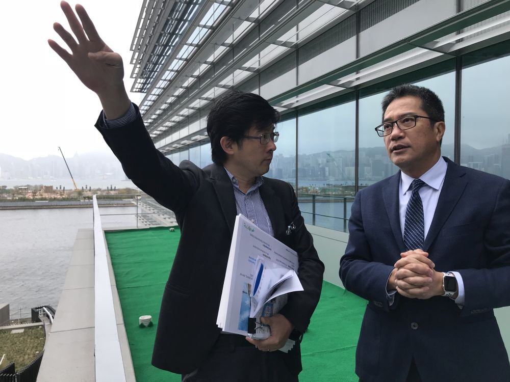 建築署總工程策劃經理李翹彥（左）向黃偉綸局長介紹外牆安裝的遮陽板，是用作減輕熱能走進大樓內。