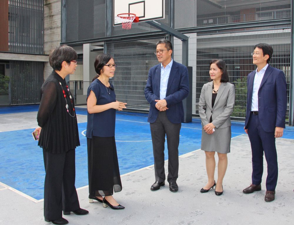 建築署高級建築師李百怡（左二）向黃偉綸局長（中）介紹，籃球場「破格地」設於一樓，在校內建築群中間，營造一個中心點，拉近學生、課室與戶外空間的距離。
