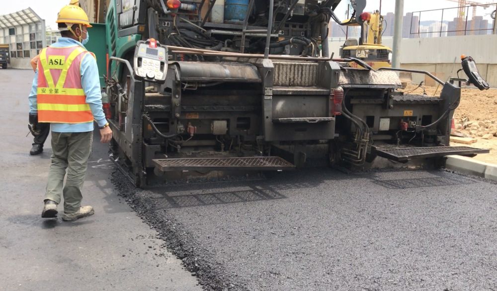 圖中工友正進行鋪設瀝青路面工程。由於內地採石場曾經停工，導致用於生產瀝青的碎石無法供應，因而影響相關工序。