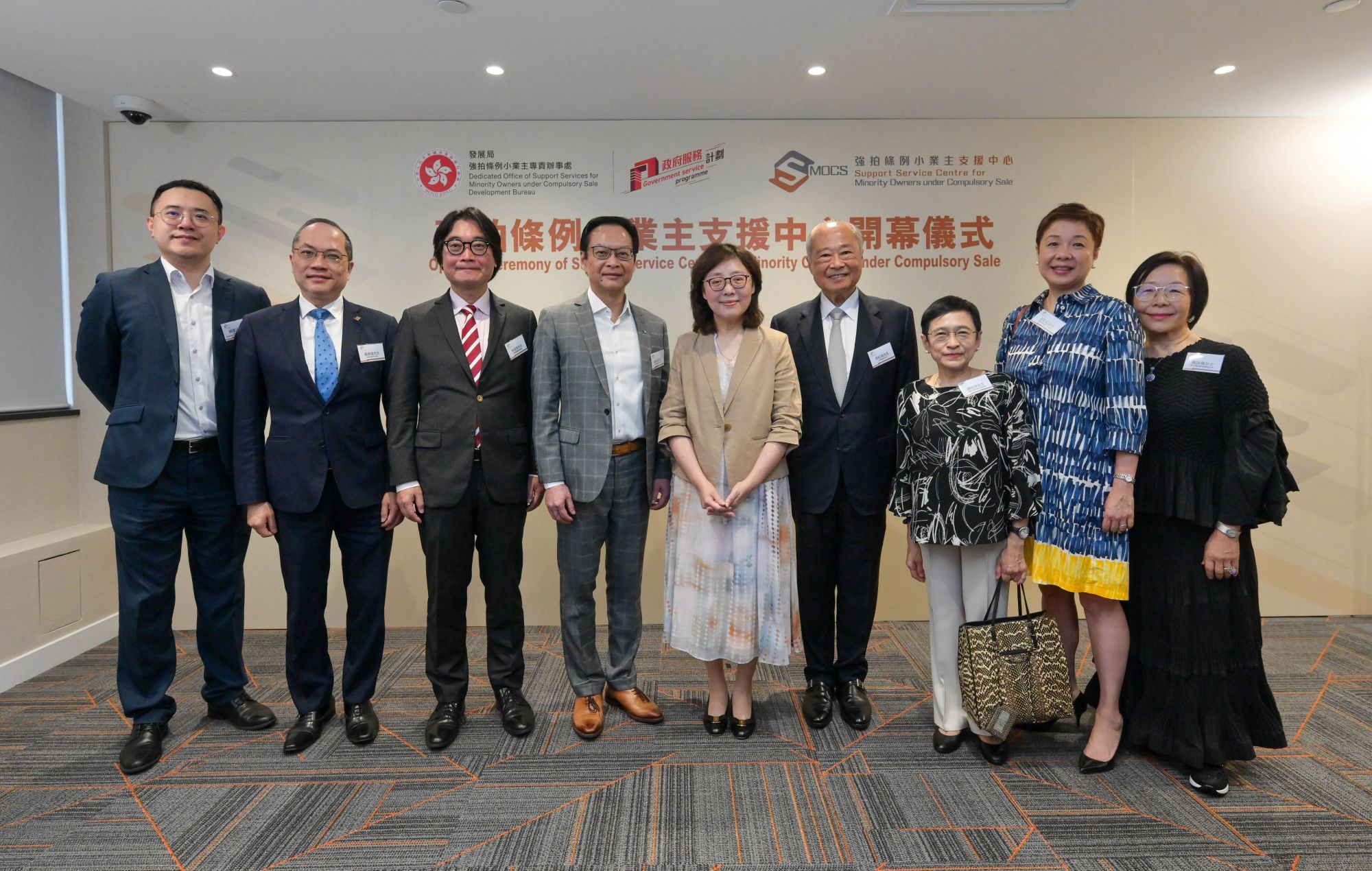 「支援中心」會透過連繫地區網絡，例如區議會、關愛隊和分區民政事務處，提升公眾及舊樓小業主對私人樓宇收購活動及強拍申請機制的認識。發展局局長甯漢豪（右四）、市區重建局主席周松崗（右三）、市區重建局行政總監韋志成（左三）、油尖旺區議會主席余健強（左二）、荃灣區議會主席區家盛（右二）、九龍城民政事務助理專員胡皓文（右一）和深水埗民政事務處高級聯絡主任鄺家權（左一）在「強拍條例小業主支援中心開幕儀式」中合照。